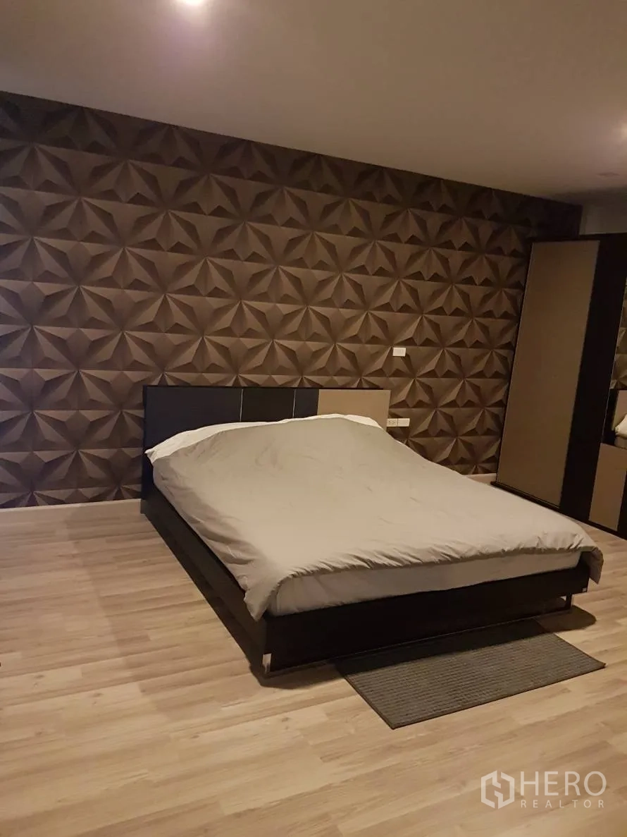 Townhouse for rent or sale in Saphan Sung, Bangkok - Second bedroom with geometric accent wall and double bed on wood floors.