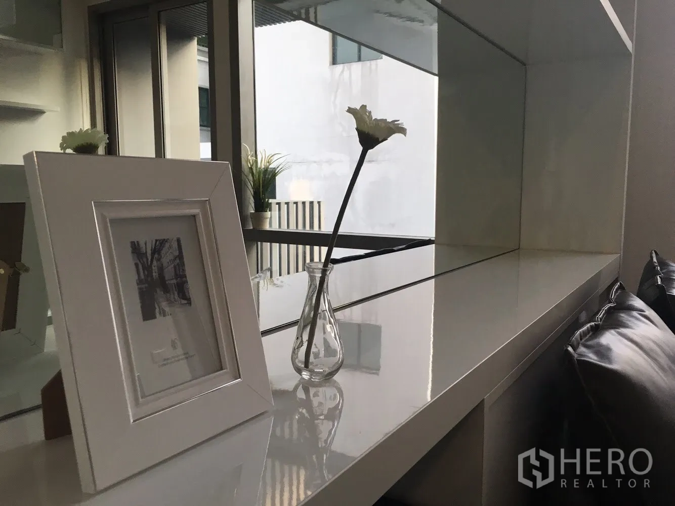 Condominium for rent in Khlong Toei, Bangkok - Close-up of mirrored shelf with picture frame and single flower vase beside the window.