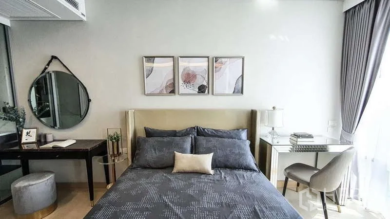 Condominium for sale in Khlong Toei, Bangkok - Cozy bedroom with upholstered headboard, three artworks, grey bedding, and a writing desk by the window.