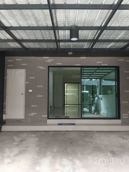 Townhouse for rent in Mueang Samut Prakan, Samut Prakan - Covered carport with metal roof and sliding glass door entry to the townhouse.