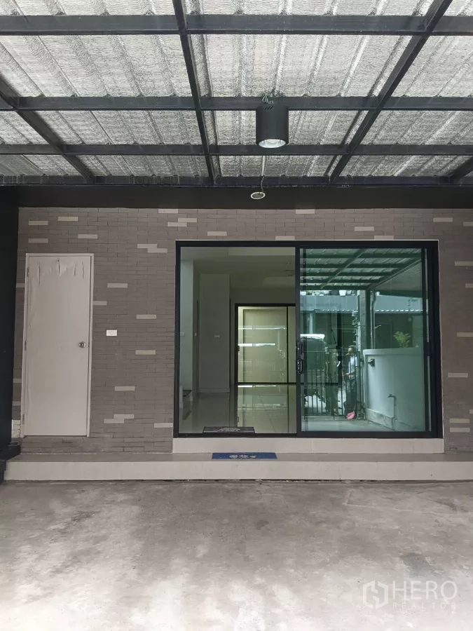 Townhouse for rent in Mueang Samut Prakan, Samut Prakan - Covered carport with metal roof and sliding glass door entry to the townhouse.