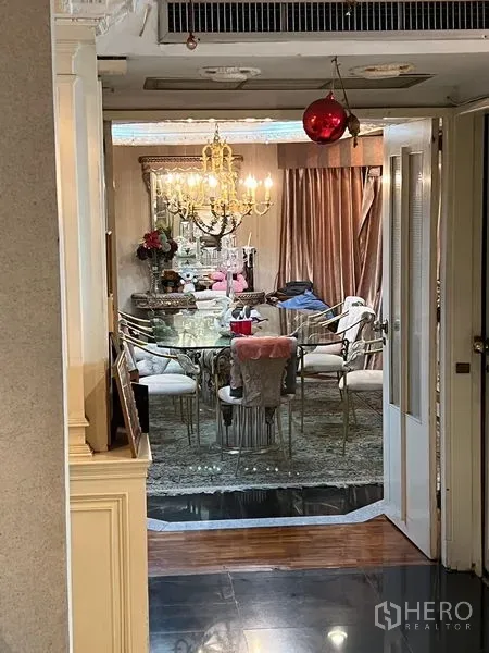 Condominium for sale in Khlong Toei, Bangkok - Formal dining room with a long glass table, gold-tone chairs and chandelier viewed through the doorway.