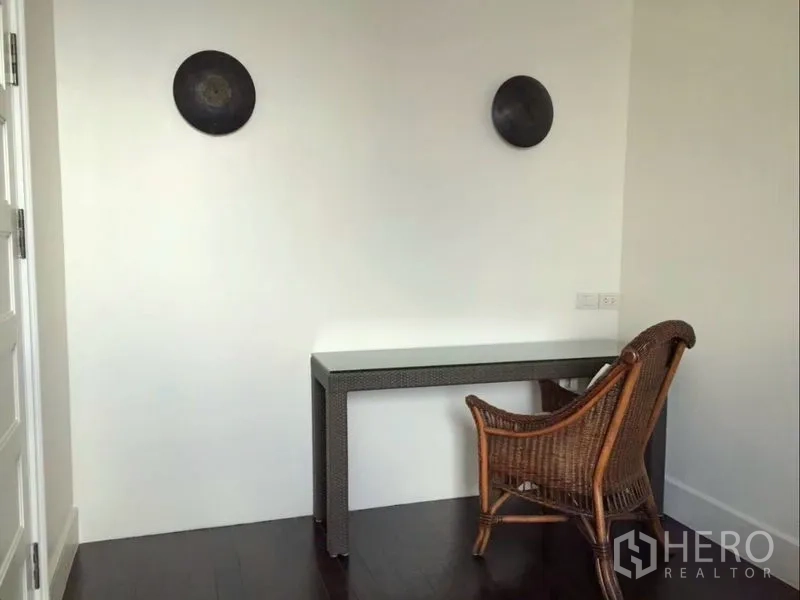 Condominium for rent in Khlong Toei, Bangkok - Minimalist study nook with rattan chair and slim desk against a white wall.