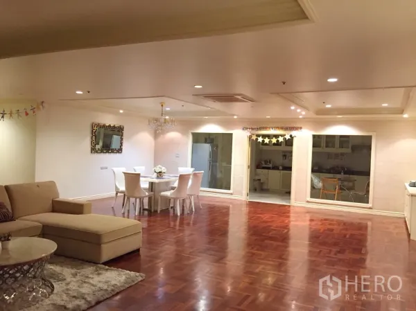 Condominium for rent in Watthana, Bangkok - Spacious open-plan living and dining area with parquet wood floors, recessed lighting, a chandelier, and interior windows looking into the kitchen.