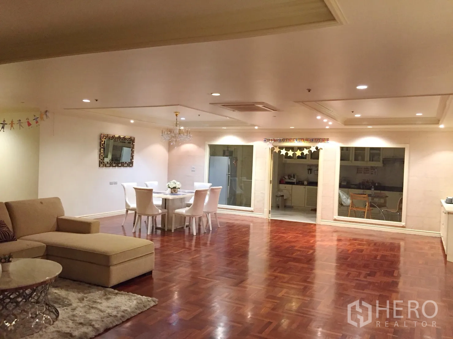 公寓 出租在Watthana, Bangkok - 开放式客餐厅，拼花木地板、嵌灯与水晶吊灯，通过内窗可看到厨房。