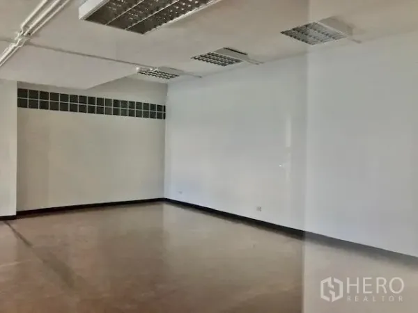Office Space for rent in Watthana, Bangkok - Bright white-walled office corner with fluorescent ceiling panels and a glass-block window strip.