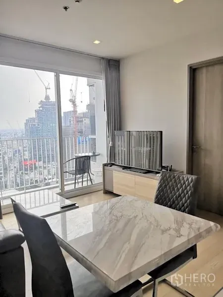 公寓 出租在Watthana, Bangkok - 用餐区与电视柜面向落地窗，通往高层阳台的城市景观。