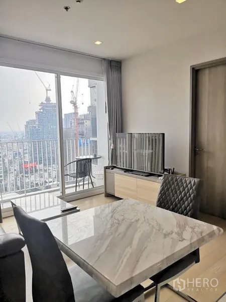 公寓 出租在Watthana, Bangkok - 用餐区与电视柜面向落地窗，通往高层阳台的城市景观。