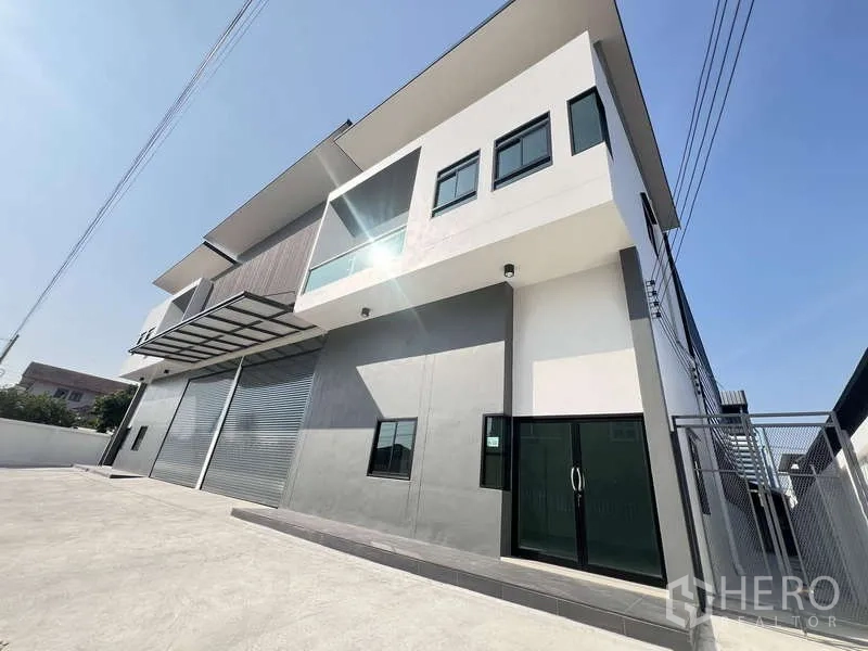 Warehouse for rent or sale - Angled view of the warehouse exterior showing a sliding glass office entrance, canopy and gated side access.