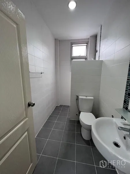 Home Office for sale in Lat Krabang, Bangkok - Long bathroom with partitioned shower, toilet, sink and gray floor tiles.