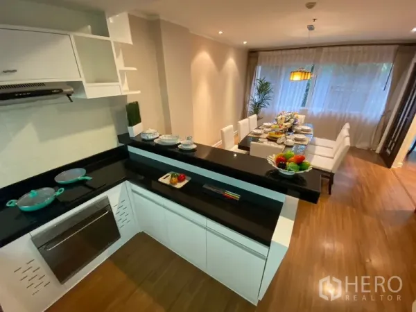 Apartment for rent in Watthana, Bangkok - U-shaped kitchen with black stone countertops and a serving bar facing the dining area.