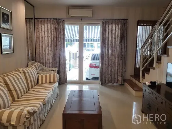 ทาวน์เฮาส์ ให้เช่าในWang Thonglang, Bangkok - ห้องนั่งเล่นโซฟาลายทาง โต๊ะกลาง และประตูกระจกเปิดสู่ที่จอดรถหน้าบ้าน