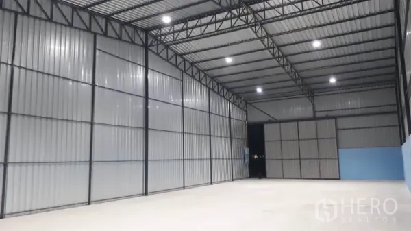 Warehouse for rent in Khlong Luang, Pathum Thani - Spacious warehouse interior with 7‑meter high ceiling, steel trusses, corrugated metal walls and bright LED lighting over smooth flooring.