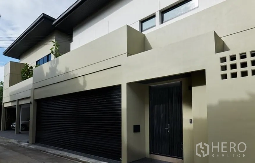 Detached House for rent in Watthana, Bangkok - Modern two-storey detached house facade with black roller garage door and solid entry gate.