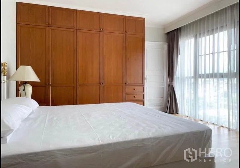 Condominium for rent in Sathon, Bangkok - Master bedroom with full-height wooden wardrobes and large balcony-style windows.