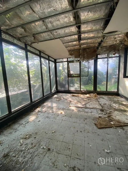 Detached House for rent in Bang Na, Bangkok - Interior glass sunroom with floor-to-ceiling windows and a damaged ceiling, overlooking the garden and trees.