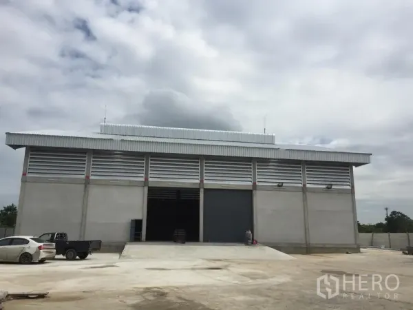 Warehouse for rent in Khlong Sam Wa, Bangkok - Modern concrete warehouse exterior with wide roller shutter doors, loading ramp and large driveway.