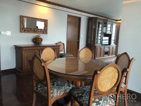Condominium for rent in Khlong Toei, Bangkok - Dining area with round glass-top table, rattan-back chairs and sideboard.