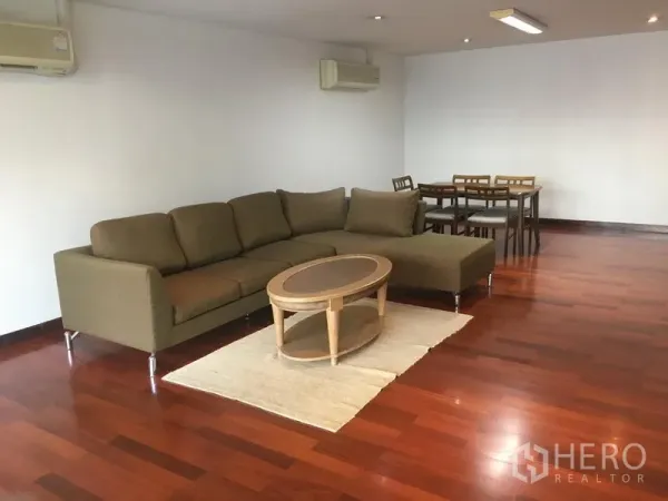 Condominium for rent or sale in Watthana, Bangkok - Spacious living room with L-shaped sofa, oval coffee table, dining set and polished hardwood floors with split air-conditioning.