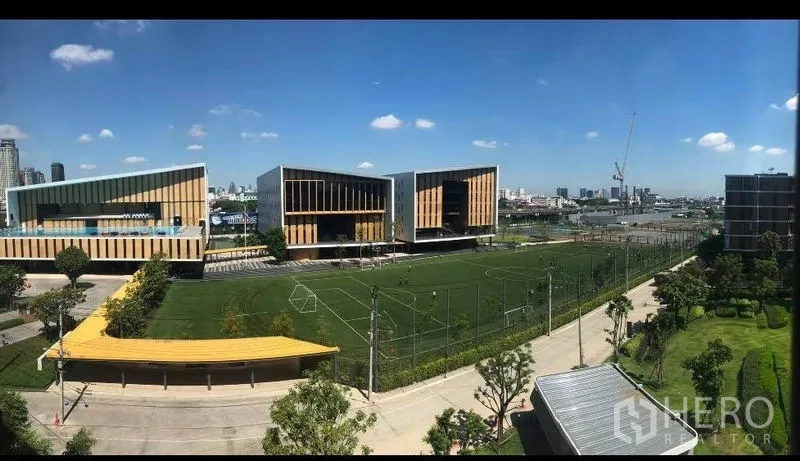 Condominium for sale in Watthana, Bangkok - View of a green football field and contemporary community buildings under a blue sky near the condo.