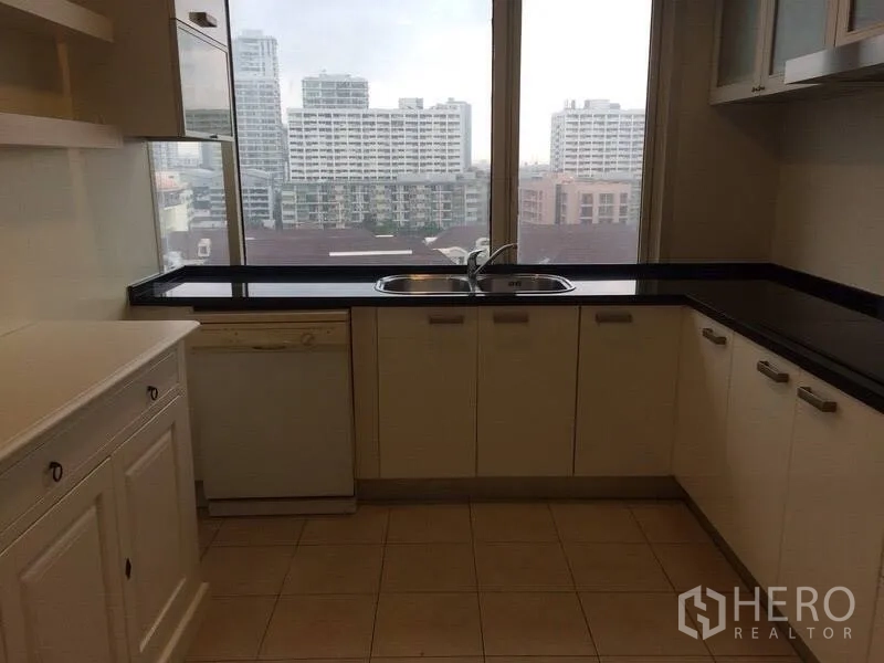 Condominium for rent in Watthana, Bangkok - Bright kitchen with white cabinets, black countertops, double sink and city view through a picture window.