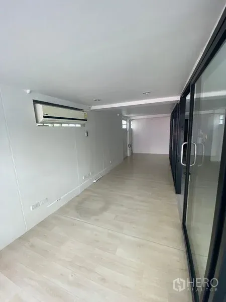 Retail Space for rent in Watthana, Bangkok - Long narrow retail interior with light wood flooring, white walls, recessed lights, glass sliding doors and wall-mounted air conditioner.