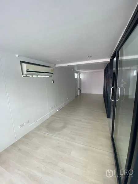 Retail Space for rent in Watthana, Bangkok - Long narrow retail interior with light wood flooring, white walls, recessed lights, glass sliding doors and wall-mounted air conditioner.