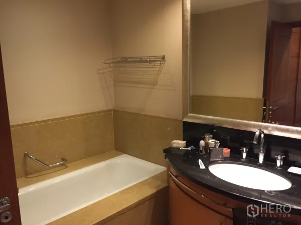 Condominium for rent in Sathon, Bangkok - Bathroom with built-in bathtub and a wide mirror over a stone countertop.