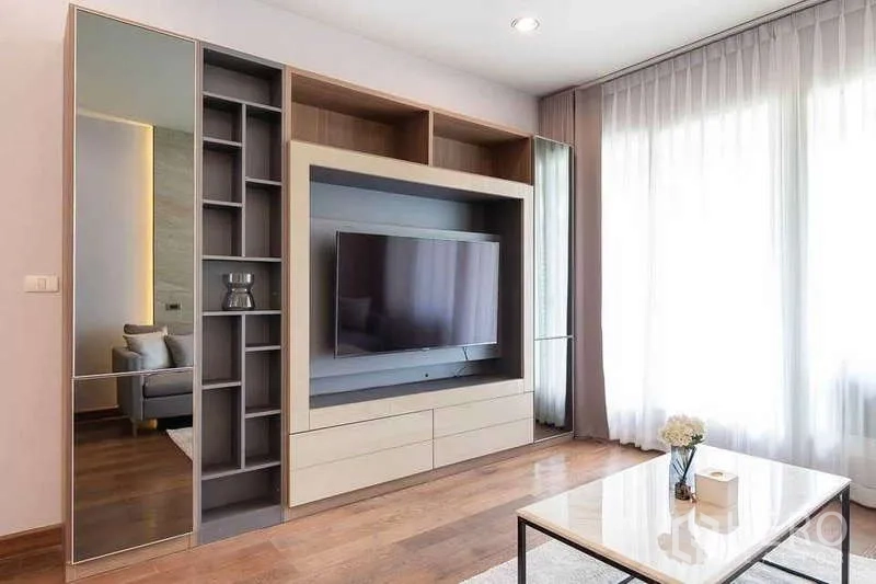 Condominium for rent in Pathum Wan, Bangkok - Living room with built-in media wall, coffee table, and sheer curtains letting in natural light.