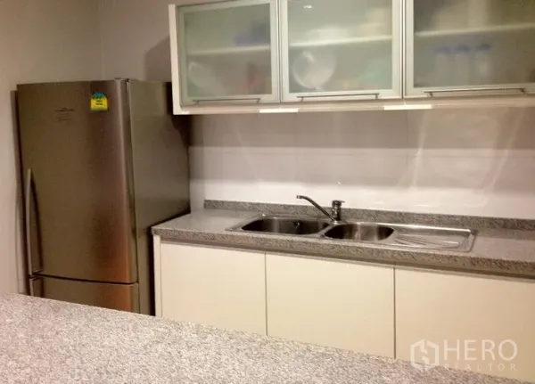 Condominium for rent in Khlong Toei, Bangkok - Kitchen corner featuring a double sink, stainless refrigerator and ample storage cabinets.