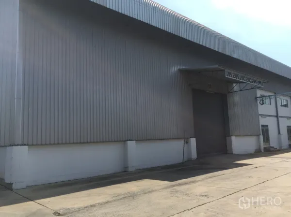 Factory for rent in Khlong Luang, Pathum Thani - Warehouse facade with a roller shutter loading door under a canopy.
