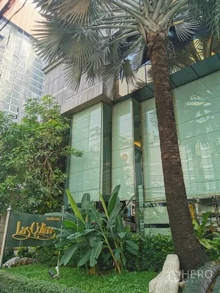 公寓 出租在Watthana, Bangkok - Las Colinas 大门景观，热带绿植、棕榈树与项目标识。