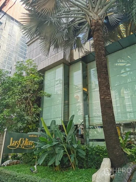 公寓 出租在Watthana, Bangkok - Las Colinas 大门景观，热带绿植、棕榈树与项目标识。