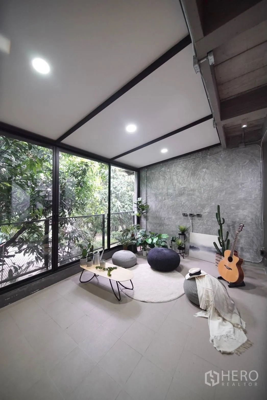 Townhouse for rent in Watthana, Bangkok - Enclosed garden room with floor-to-ceiling windows, concrete wall, plants, poufs and a guitar.
