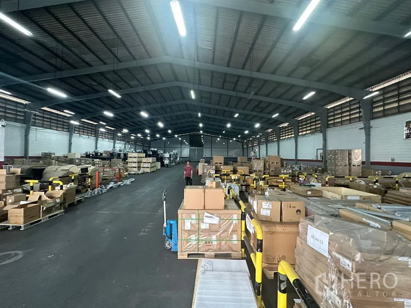 货栈 出租在Khlong Toei, Bangkok - 宽阔仓库通道，钢桁架屋顶下，托盘与货箱有序摆放于护栏旁。
