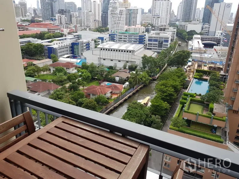 Condominium for rent in Ratchathewi, Bangkok - High-floor balcony view of city buildings, pool deck and the tree-lined canal below.