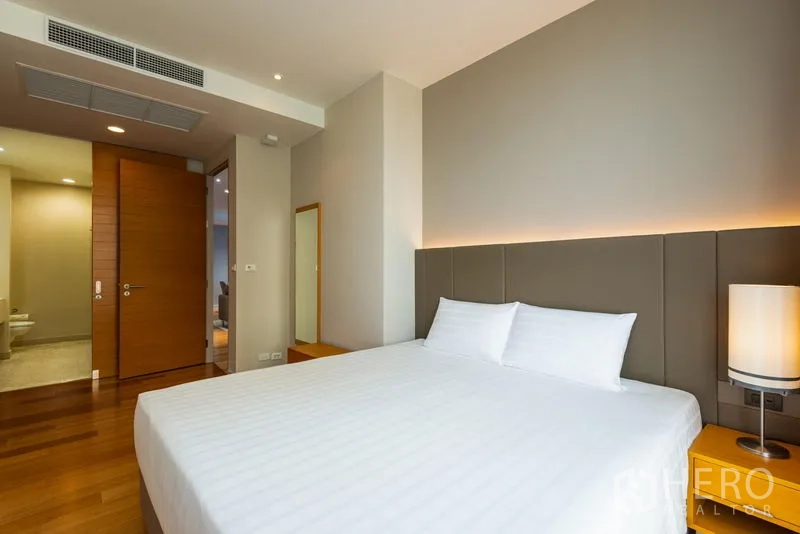Condominium for rent in Bang Kho Laem, Bangkok - Primary bedroom with king bed, warm backlit headboard, wood floors and view to an en-suite bathroom.