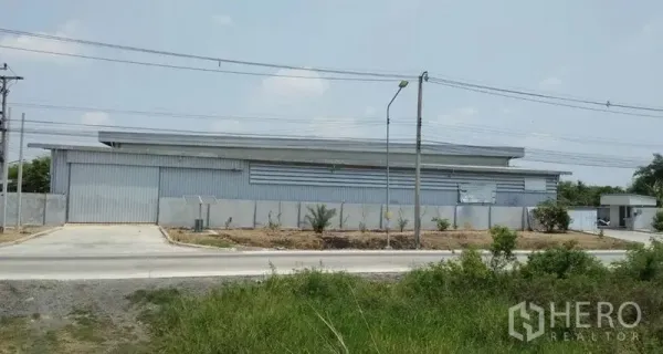 Warehouse for rent in Pathum Thani - Corner view of the warehouse exterior with a wide gate and driveway.