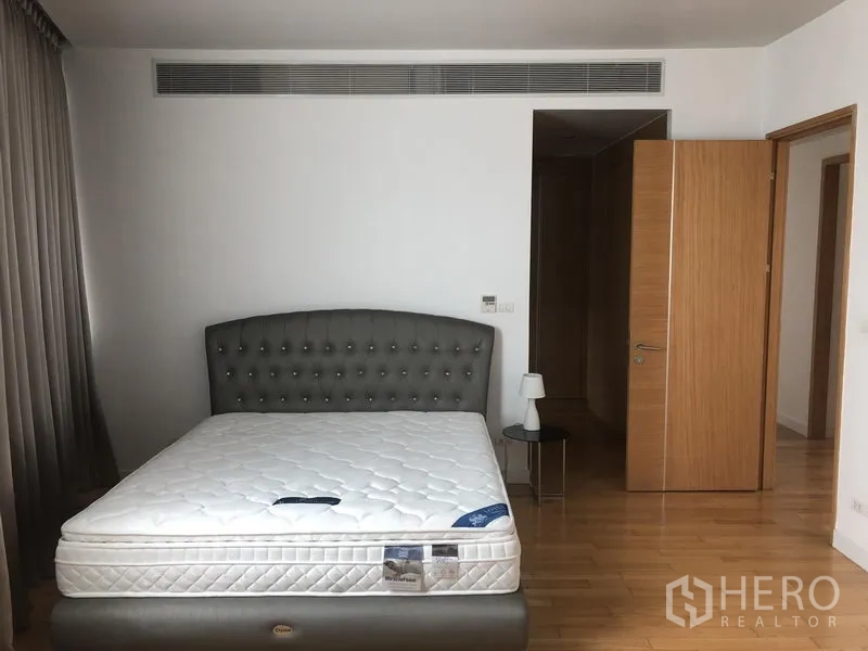 Condominium for rent in Khlong Toei, Bangkok - Spacious master bedroom with upholstered headboard, bedside tables and wood floors.