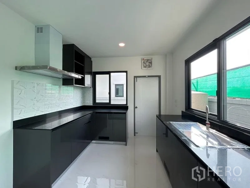 Detached House for rent - Sleek kitchen with black cabinetry, range hood, and large corner windows.