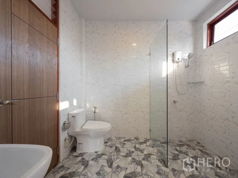Detached House for sale in Chatuchak, Bangkok - Bathroom with glass shower screen, white textured wall tiles and patterned floor tiles.