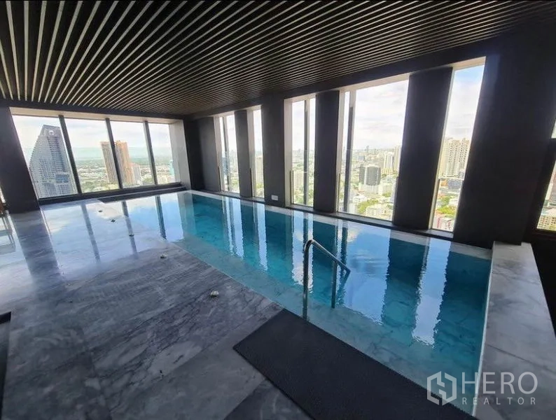 Condominium for rent in Khlong Toei, Bangkok - Indoor sky pool with tall windows and expansive city views.