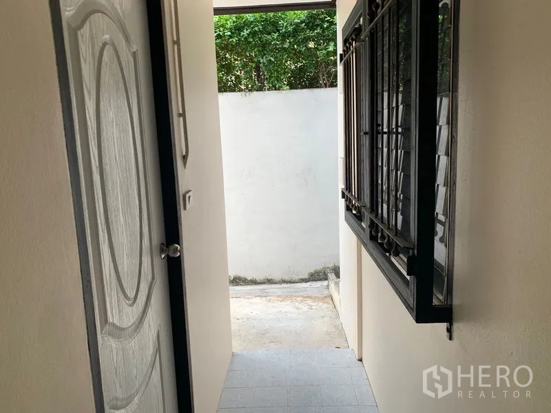 Detached House for rent in Khlong Toei, Bangkok - Narrow side corridor with security-grilled window and a door opening to a small yard.