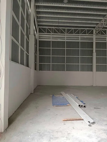 Warehouse for rent in Khlong Toei, Bangkok - High-ceiling warehouse interior with steel trusses, corrugated walls and unfinished concrete floor with materials on site.