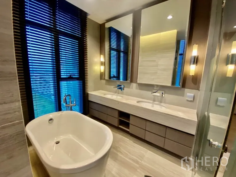 Condominium for rent or sale in Bang Rak, Bangkok - Luxurious bathroom with freestanding bathtub, double vanity, tall windows and warm lighting.