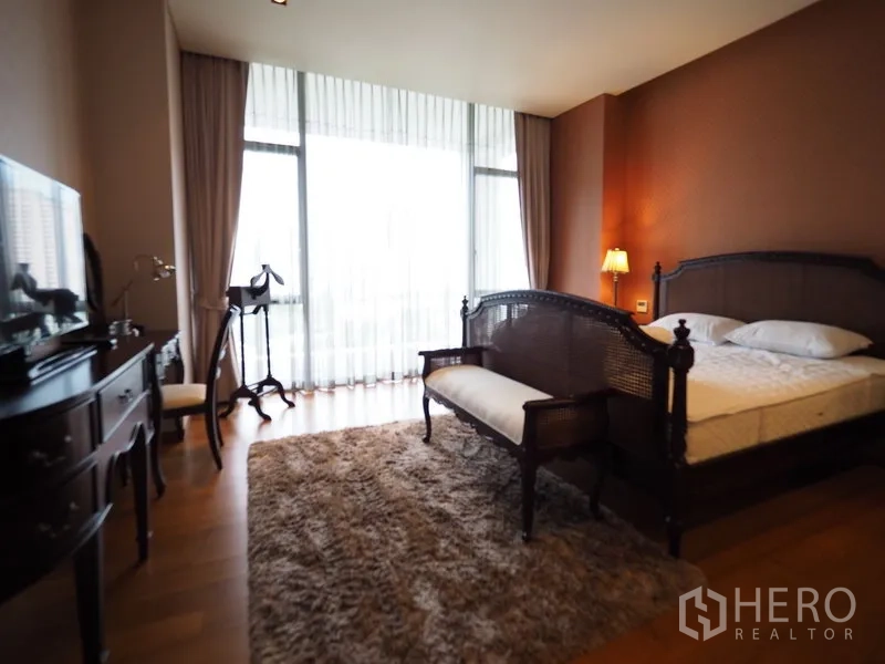 Condominium for rent in Sathon, Bangkok - Spacious bedroom with matching wooden bed and bench facing floor-to-ceiling glass.