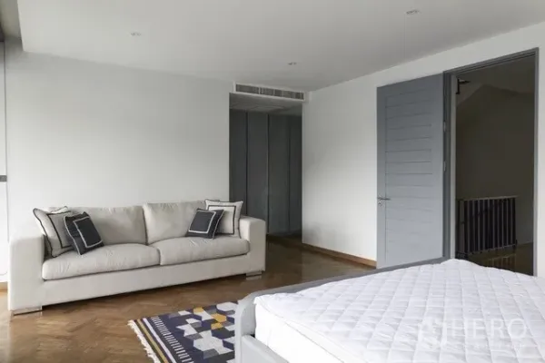 Townhouse for sale in Watthana, Bangkok - Spacious bedroom with a sofa, built-in wardrobes and parquet flooring.