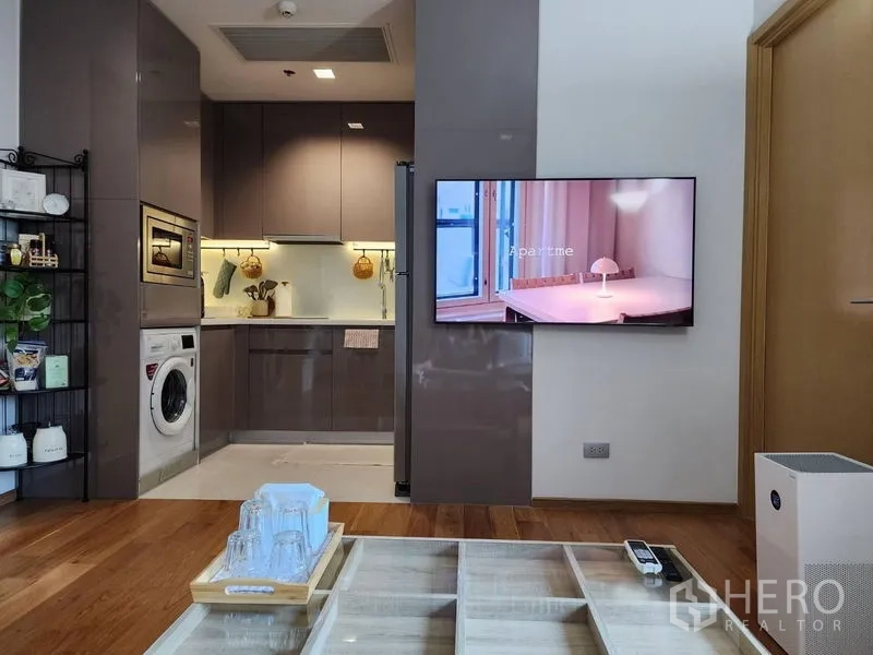Condominium for rent in Watthana, Bangkok - Open-plan living area facing a glossy L-shaped kitchen and mounted TV.