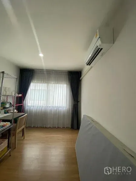 Townhouse for rent or sale in Saphan Sung, Bangkok - Bright room with wood flooring, wall-mounted air conditioner and a window with sheer and blackout curtains.