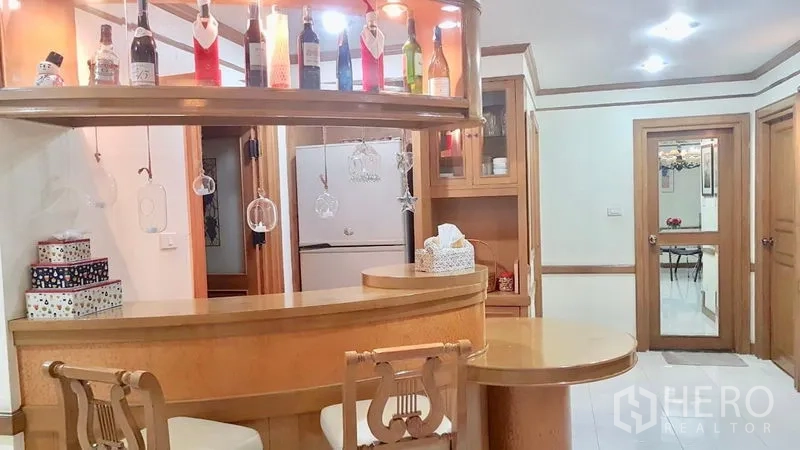 公寓 出租在Watthana, Bangkok - 弧形吧台，悬挂酒杯架与高脚椅，通向厨房的视角。